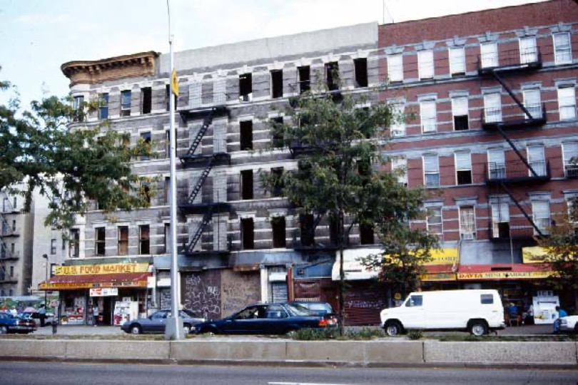 A street in Harlem, New York City. There is a five-story building in the background and cars in the midground.
